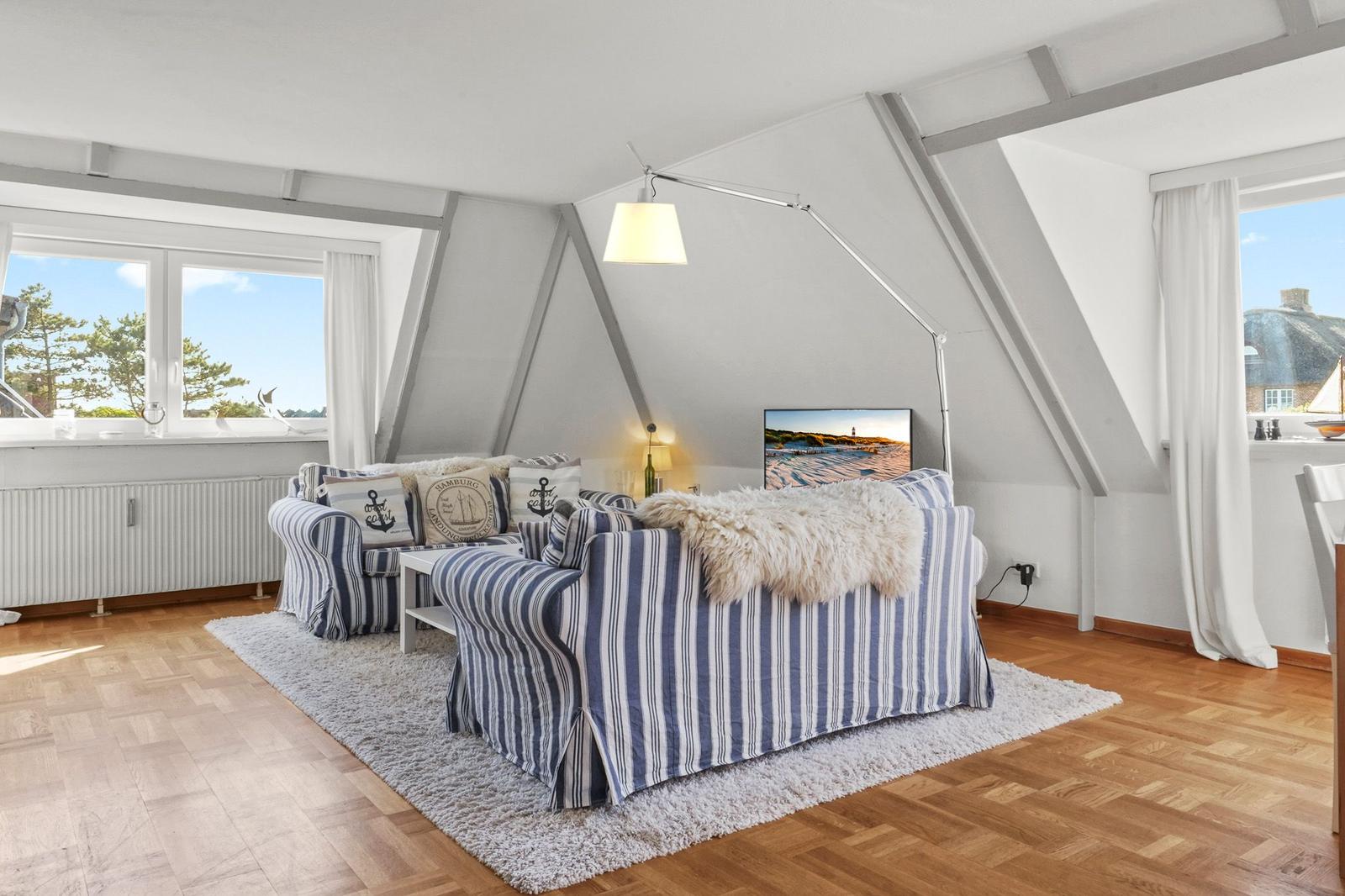 Wohnzimmer mit Sofa, Fernseher und großen Fenstern.