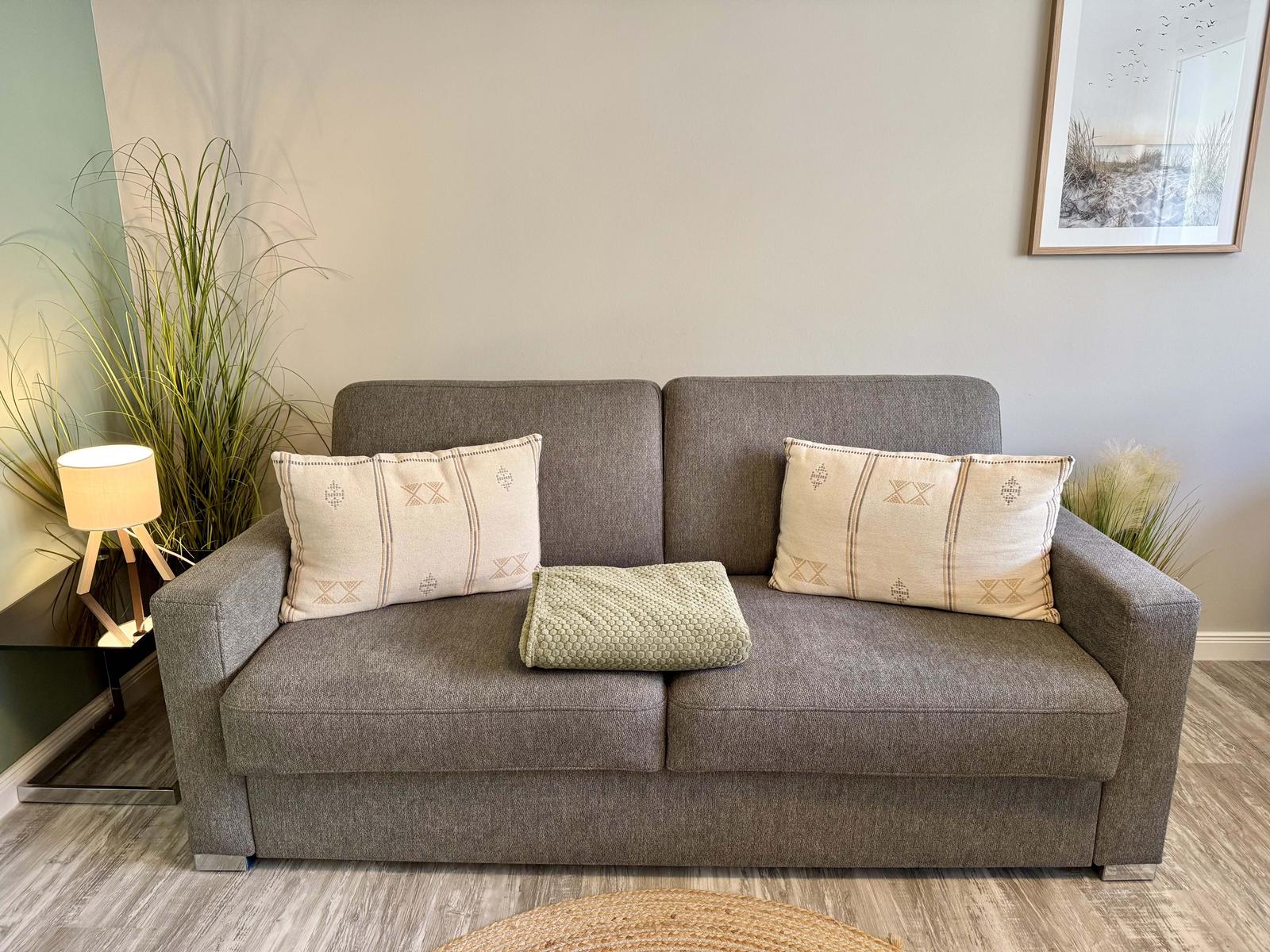 Ein grauer Sofa mit zwei Kissen und einer Decke.