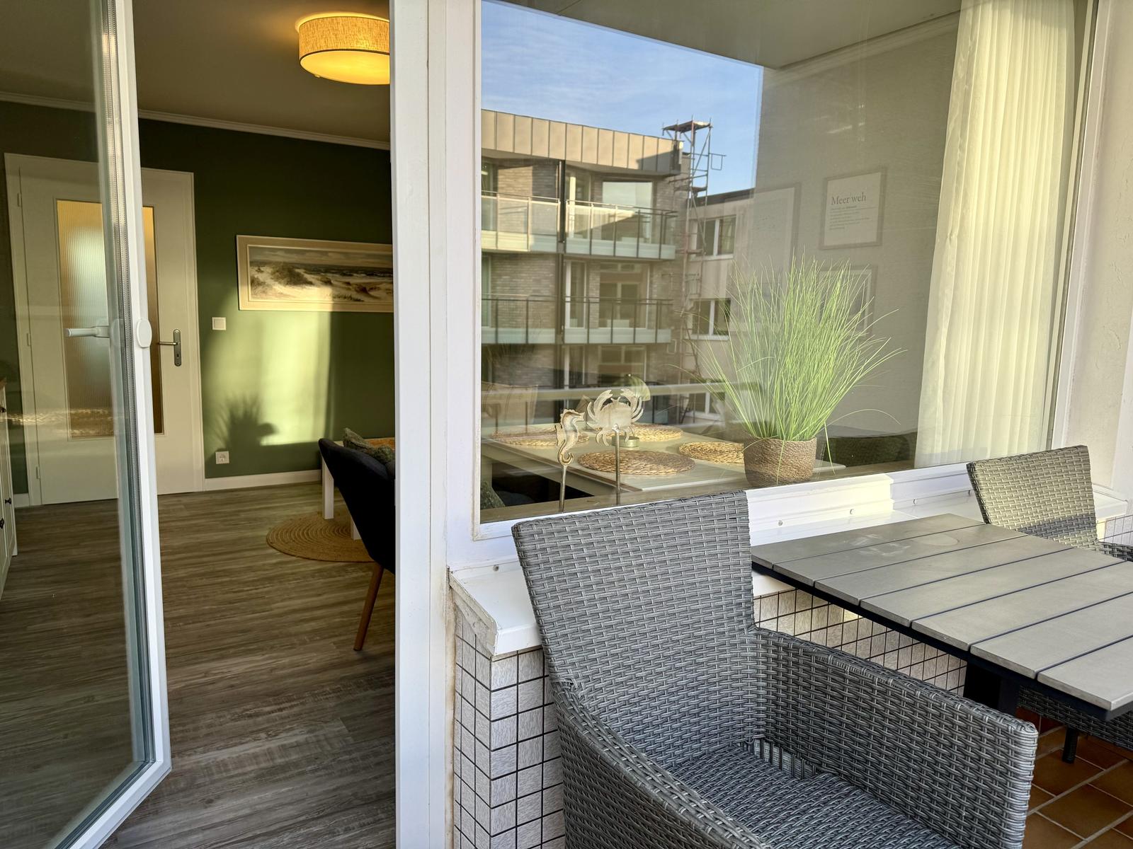 Terrasse mit Tisch und Stühlen. Blick ins Innere mit grünem Wandbereich.