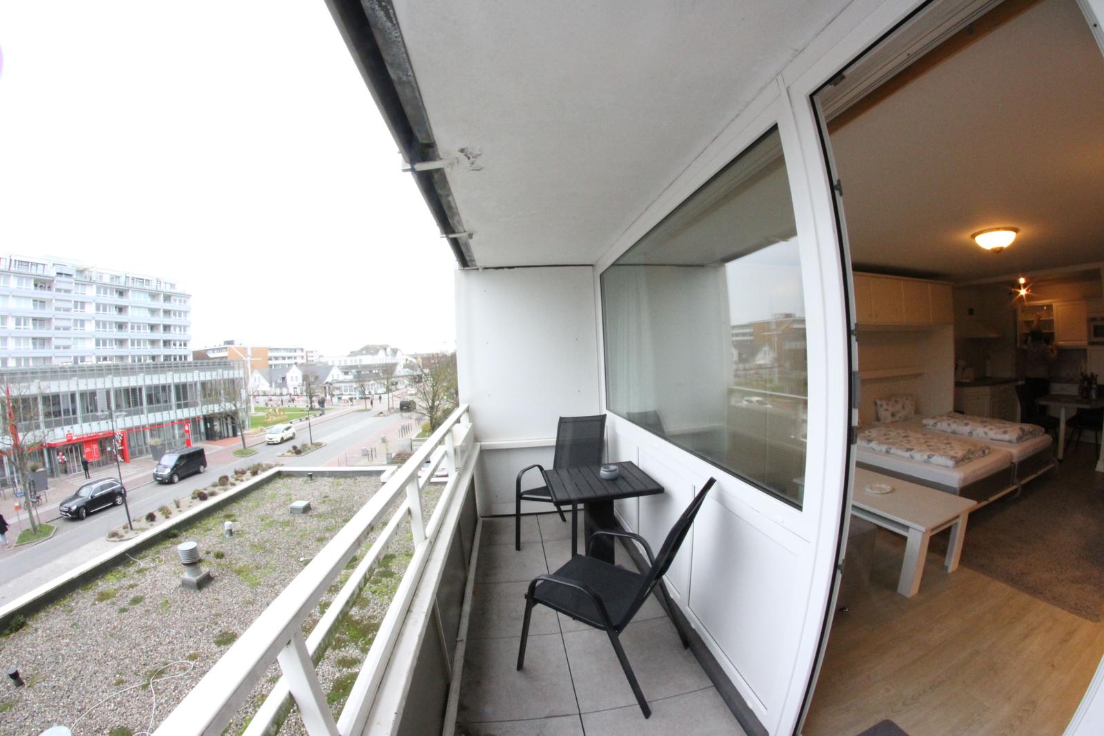 Balkon mit Tisch und Stühlen. Blick auf Straße und Gebäude.