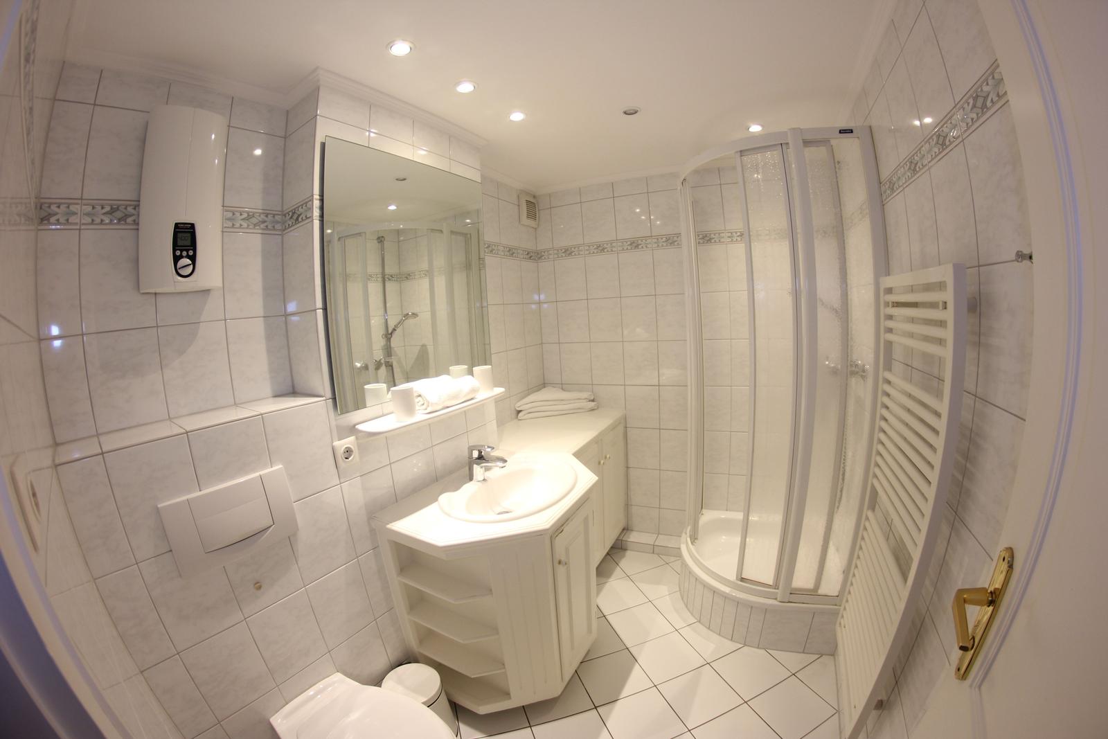 Badezimmer mit Dusche, Waschbecken und Toilette. Weiße Fliesen und Spiegel.