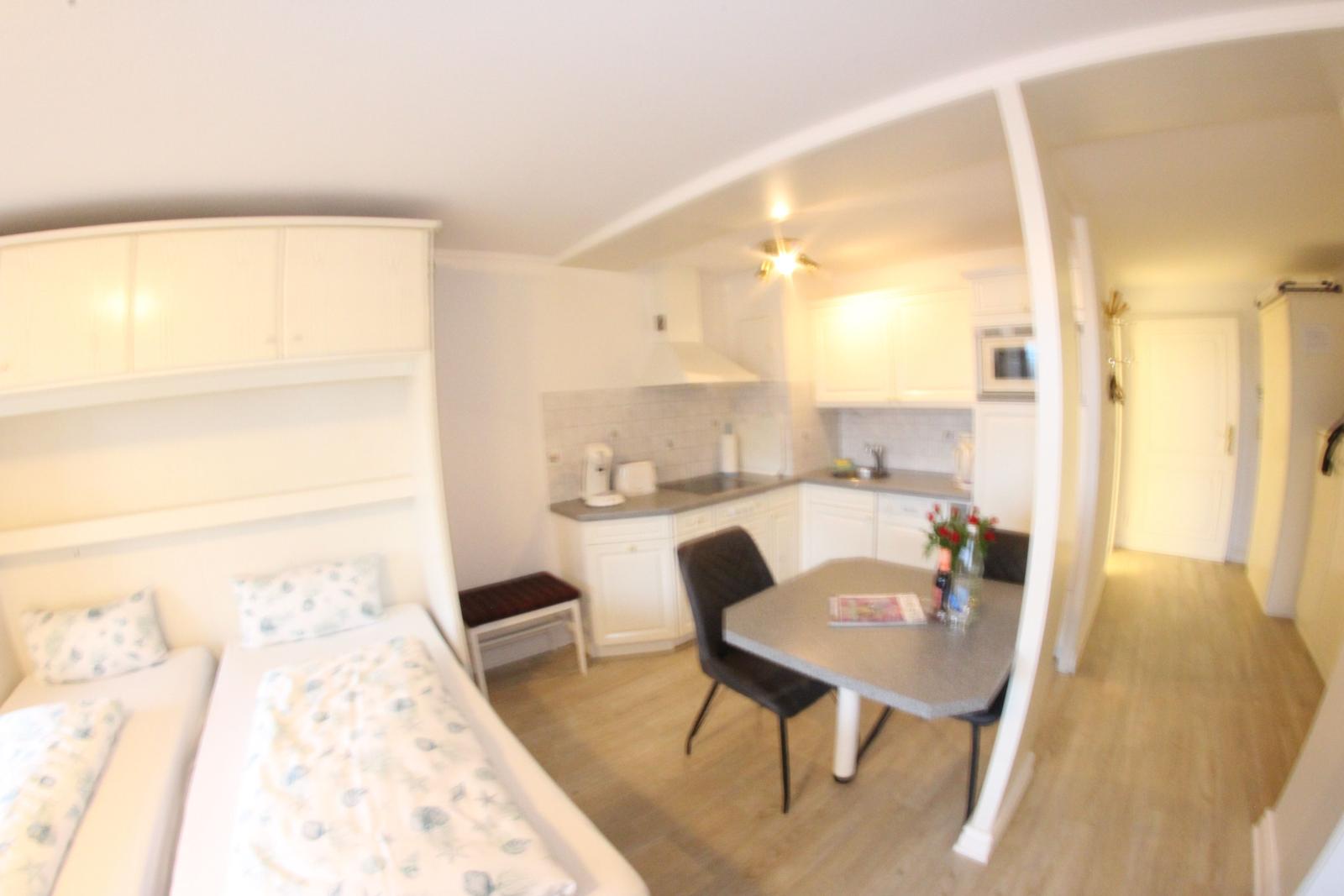 Küche mit Esstisch, Schlafbereich mit zwei Betten und weißer Einbauküche.