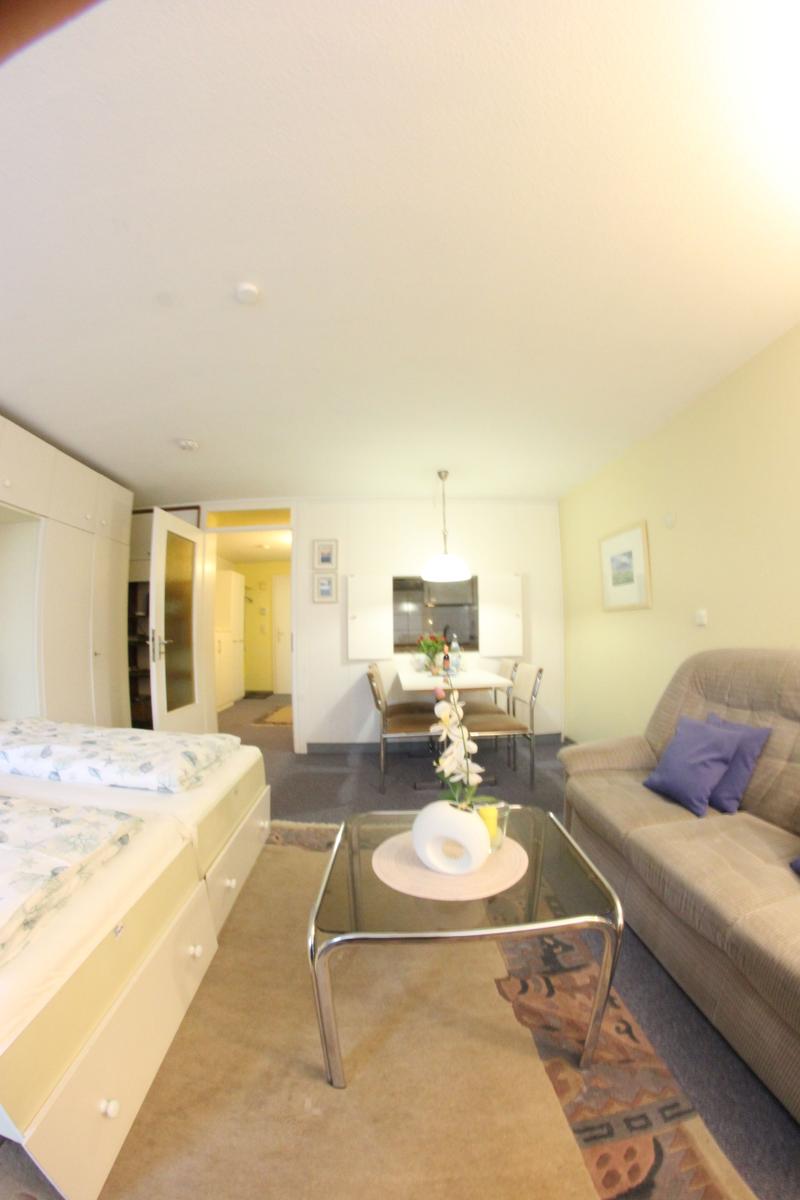 Wohnung mit Schlafzimmer, Sofa und Essbereich. Glas-Tisch mit Blumen.