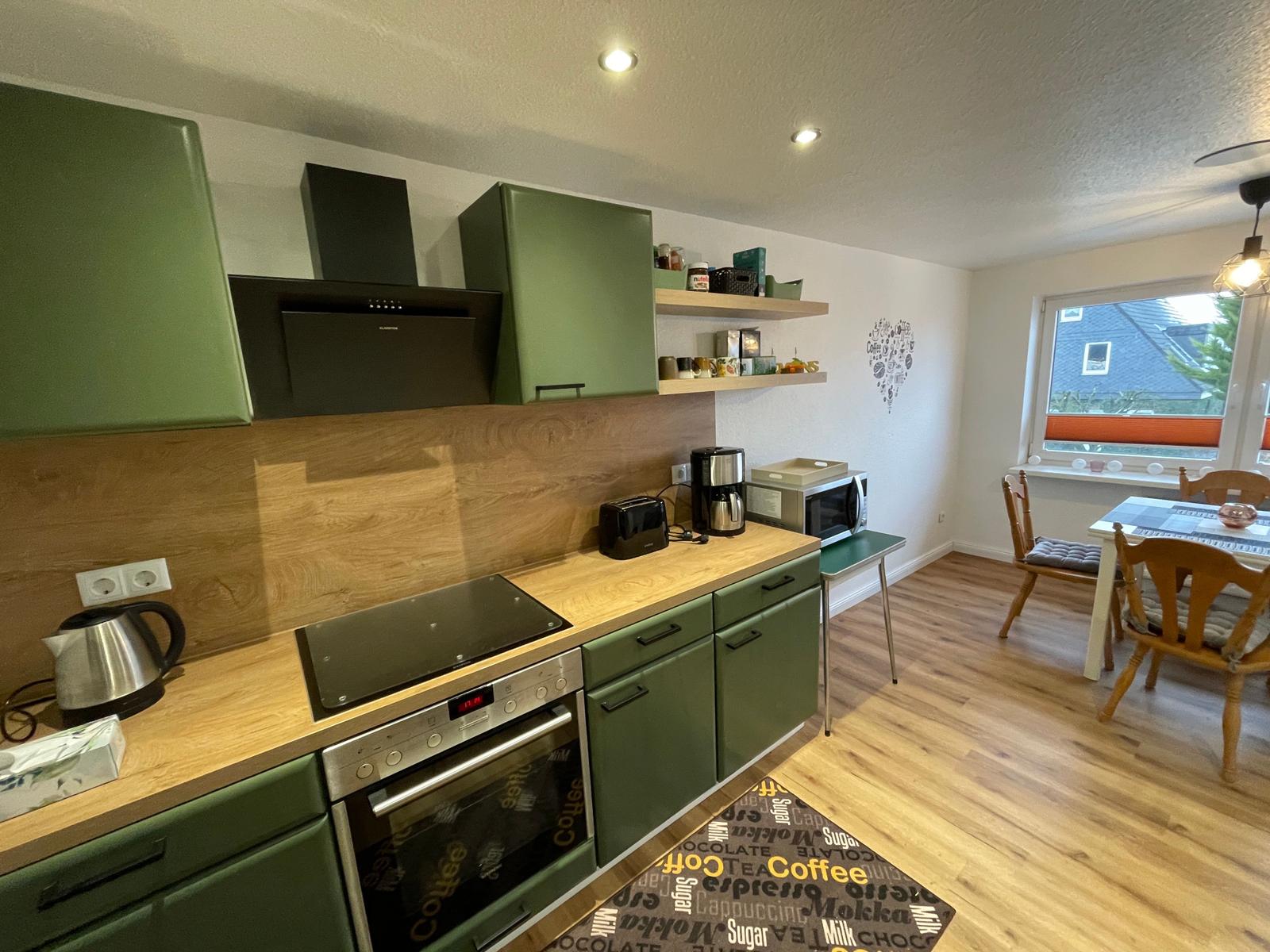 Küche mit grünen Schränken und Essbereich mit Tisch und Stühlen.