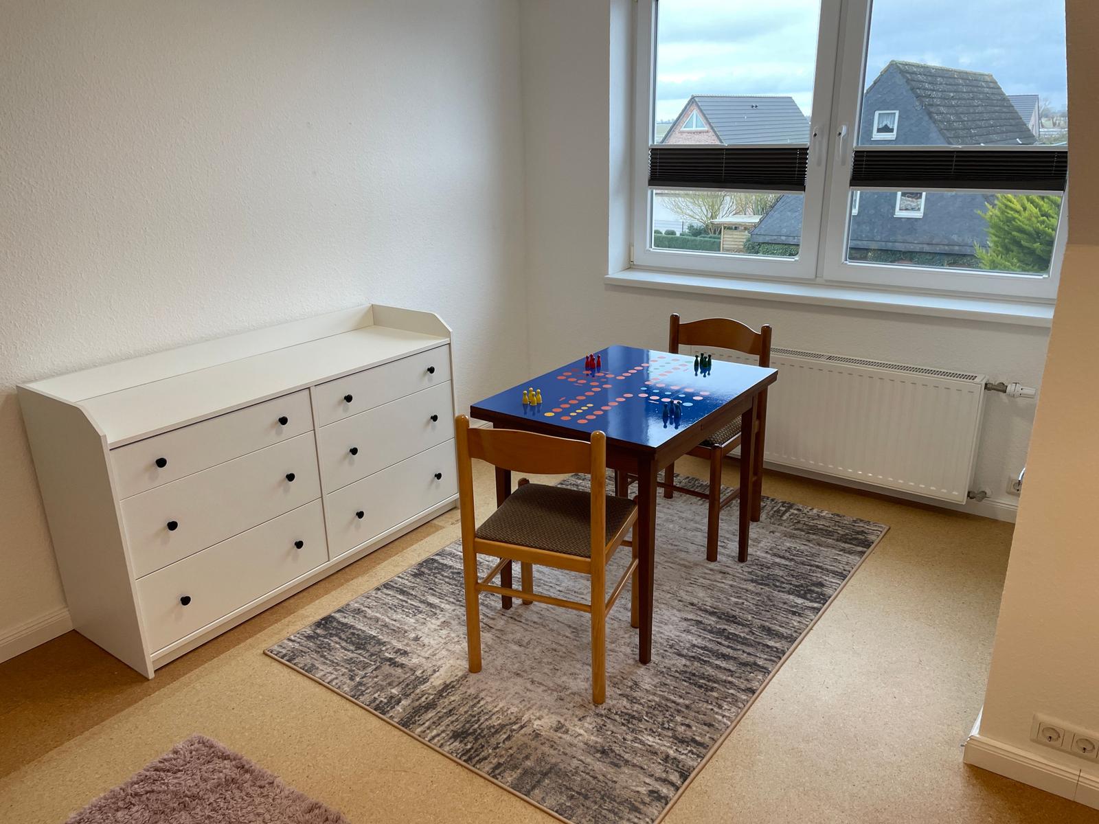 Ein Raum mit Tisch, Stühlen und Schrank. Fenster mit Blick auf Häuser.