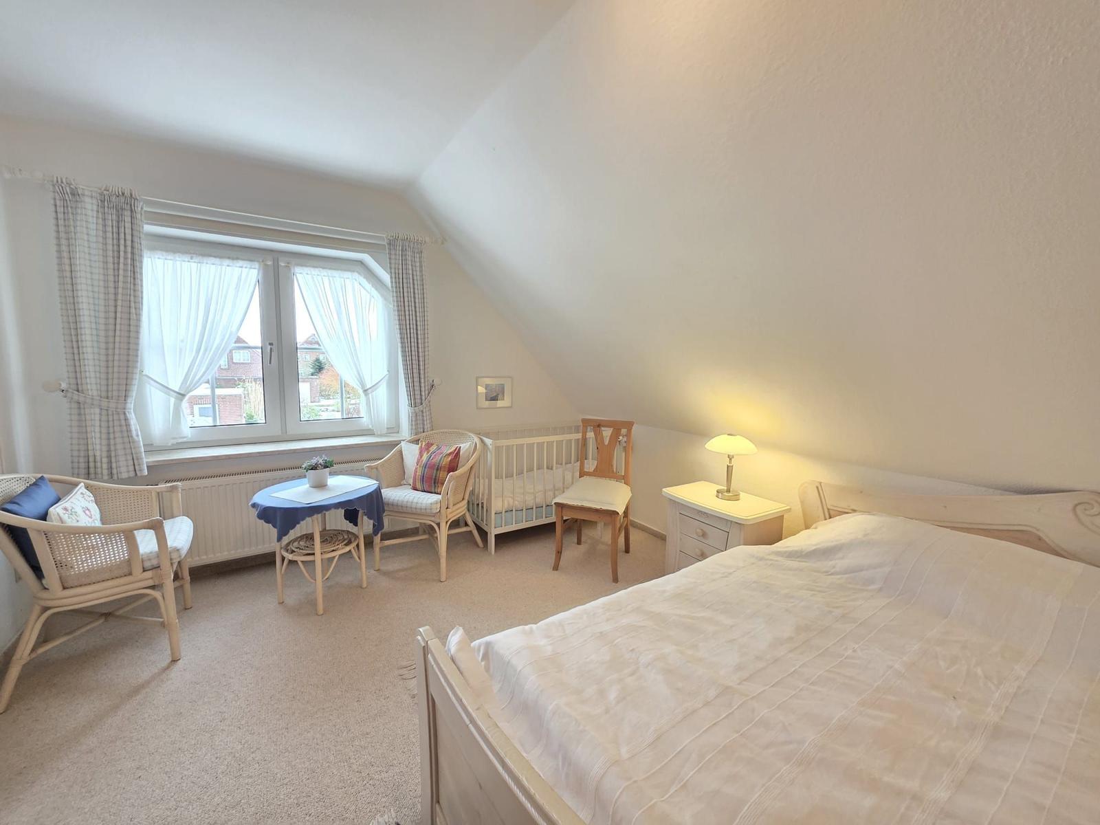 Bedroom with sloped ceiling, bed, crib, table and chairs.