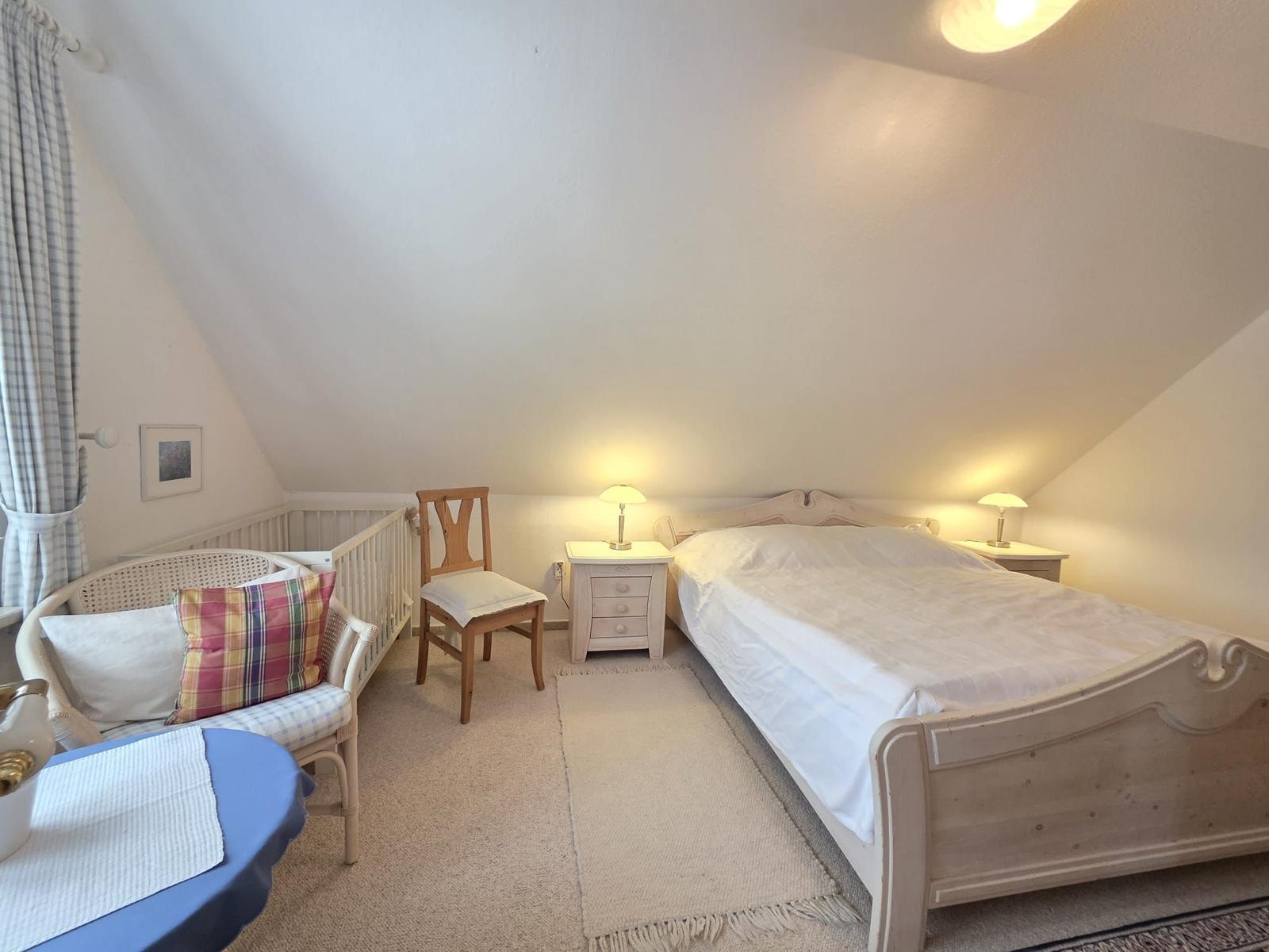 Bedroom with sloped ceiling, bed, nightstand, and chair.