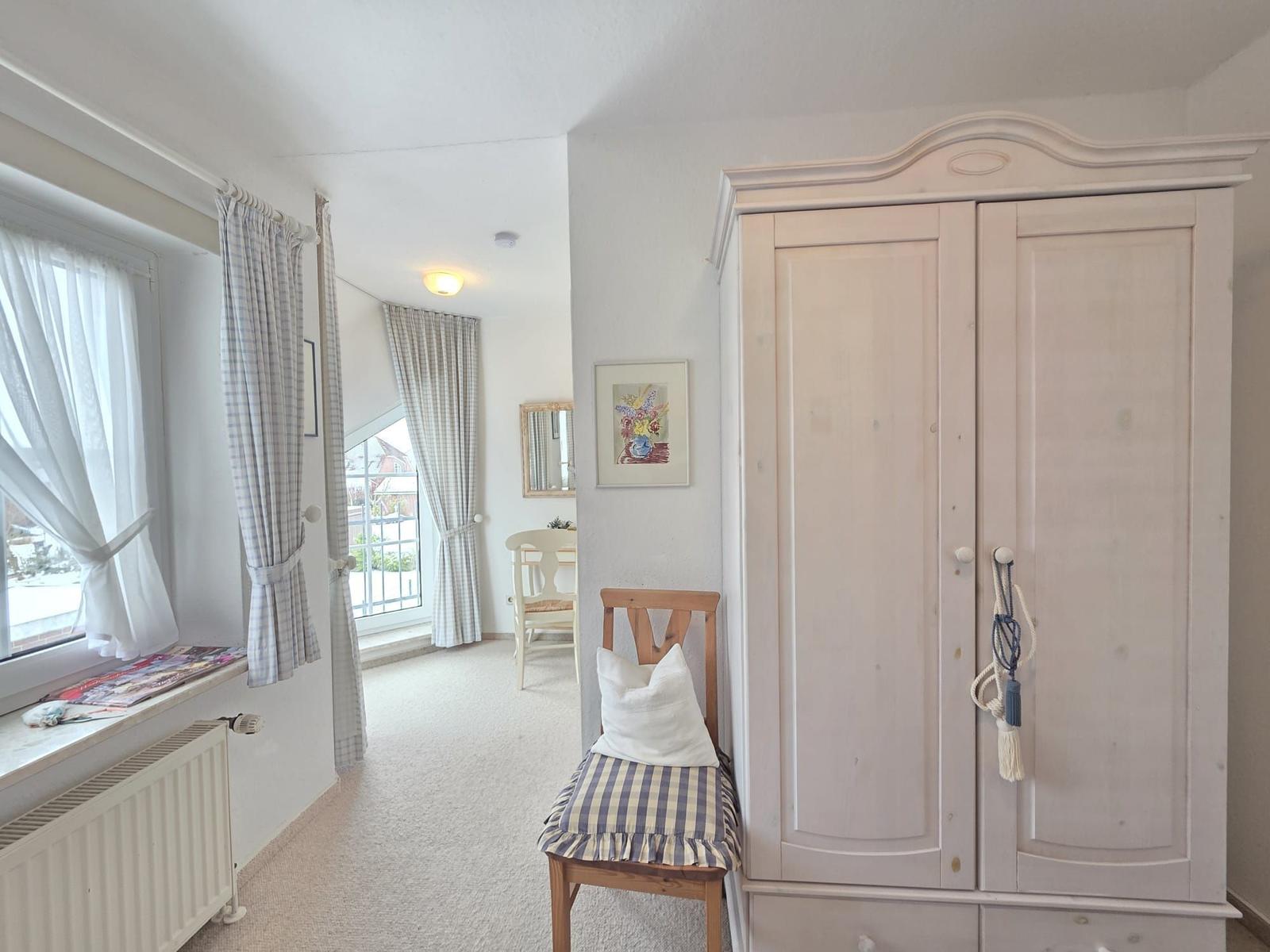 Bedroom with wardrobe, chair, and windows with curtains.