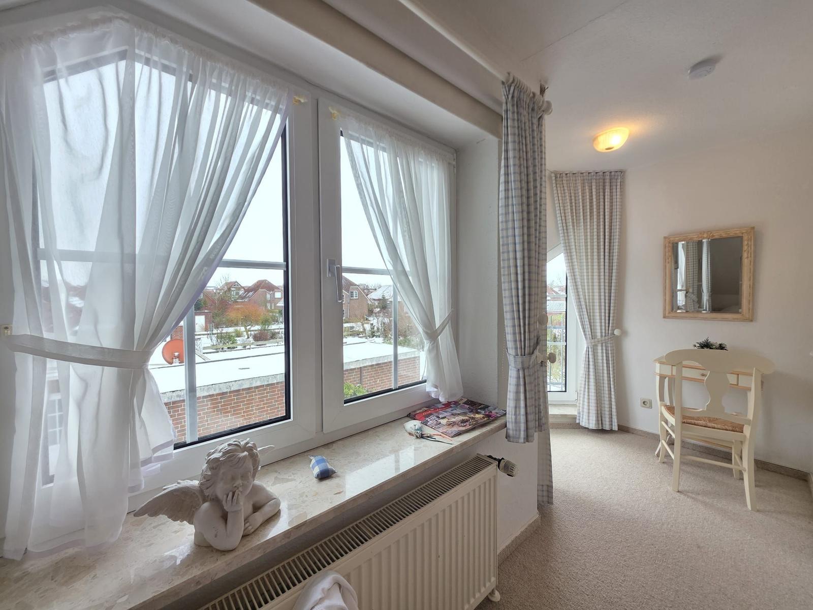 Room with large window, curtains, and desk with mirror.