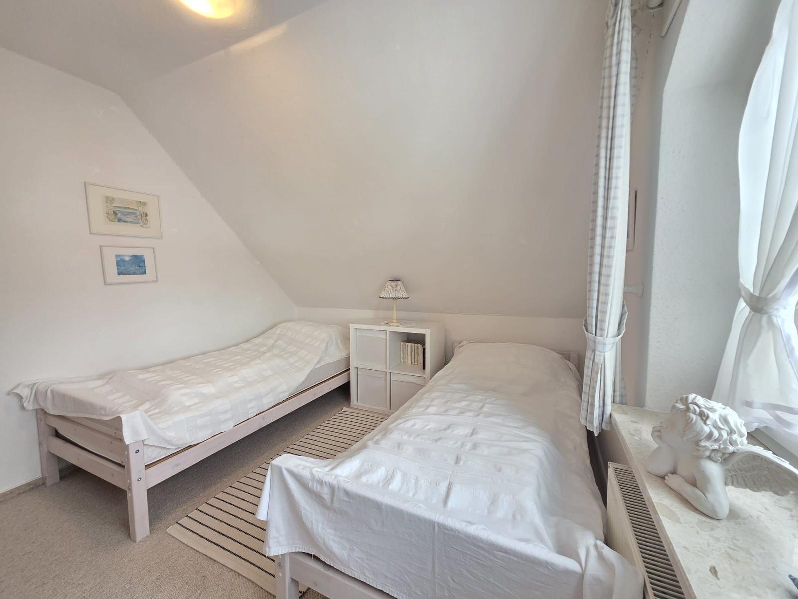 Two beds in an attic room with window and nightstand.