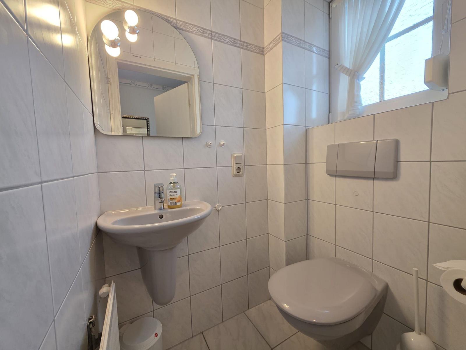 Bathroom with sink, mirror, toilet, and window.