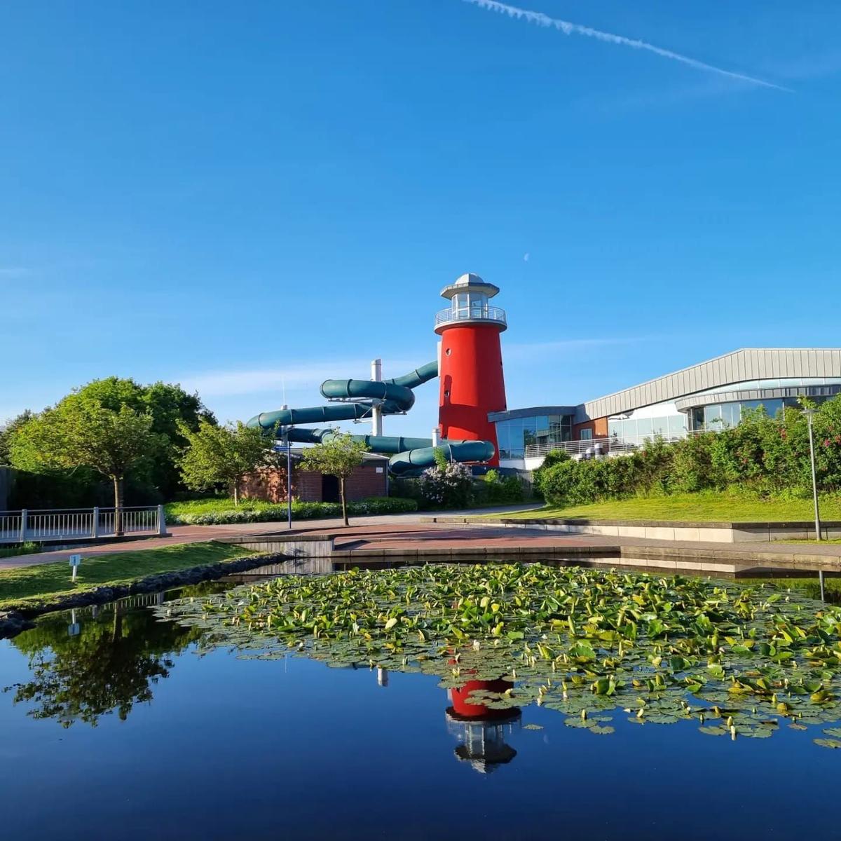 Red lighthouse with water slides beside a pond with water lilies.