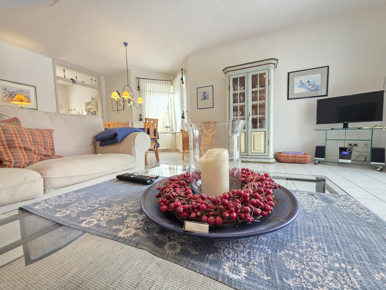 Living room with sofa, coffee table, and TV. Decor with red berries and candle.