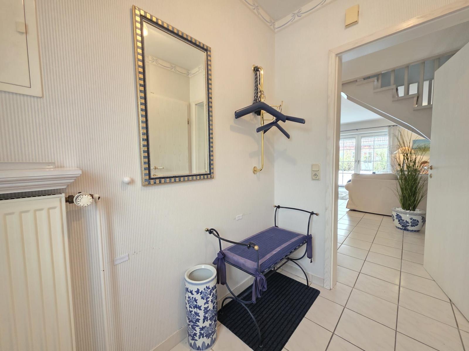 Entrance with mirror, bench, and coat rack. View into living room with sofa and plant.