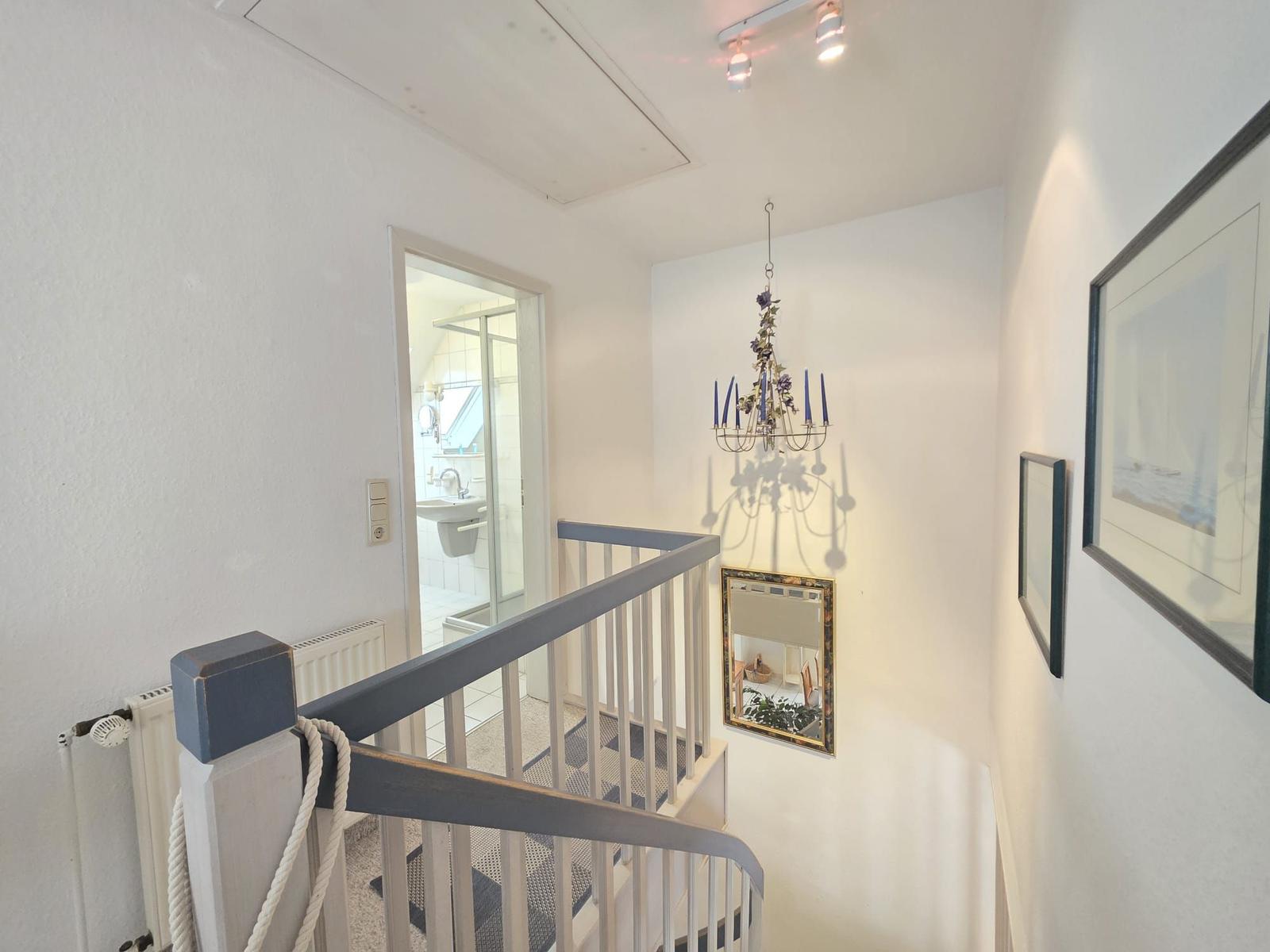 Staircase with mirror, chandelier, and view into bathroom.