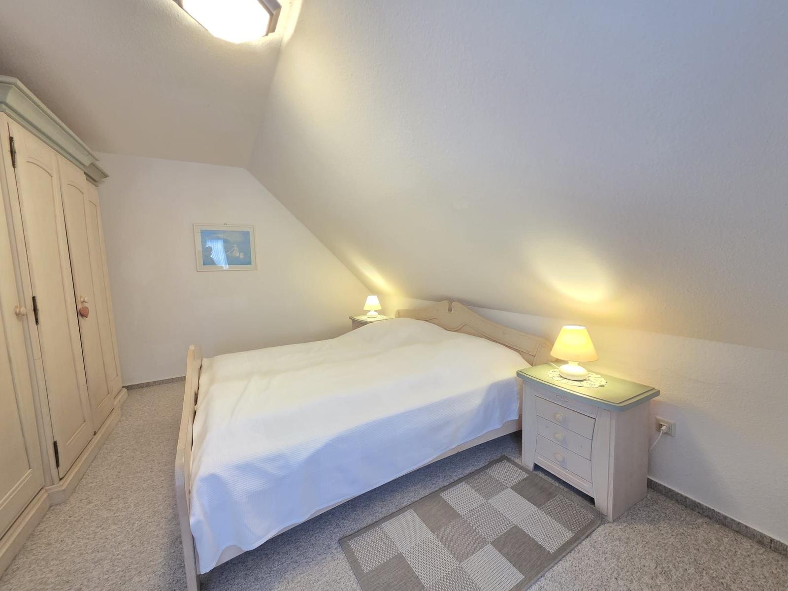 Bedroom with sloped ceiling, bed, nightstand, and wardrobe.