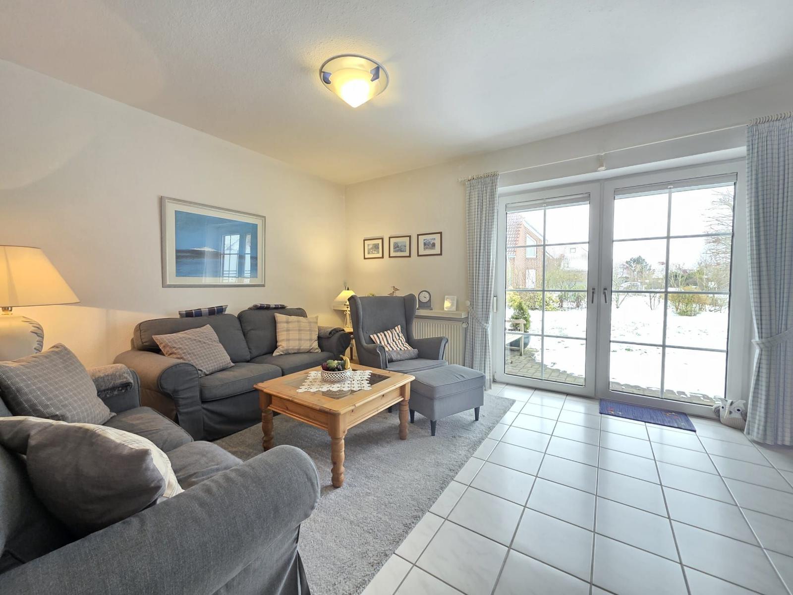 Living room with sofa, armchair, and glass door to the garden.