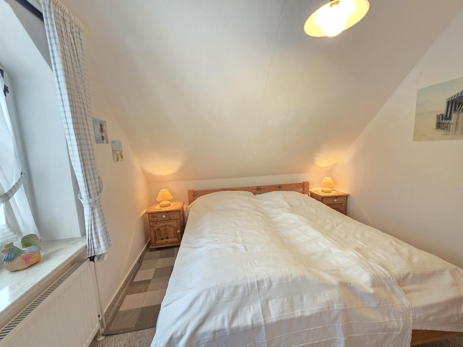 Bedroom with sloped ceiling, bed, two nightstands, and window with curtain.