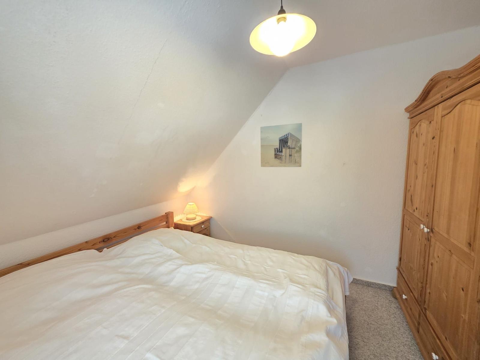 Bedroom with bed, wardrobe, and nightstand under sloped ceiling
