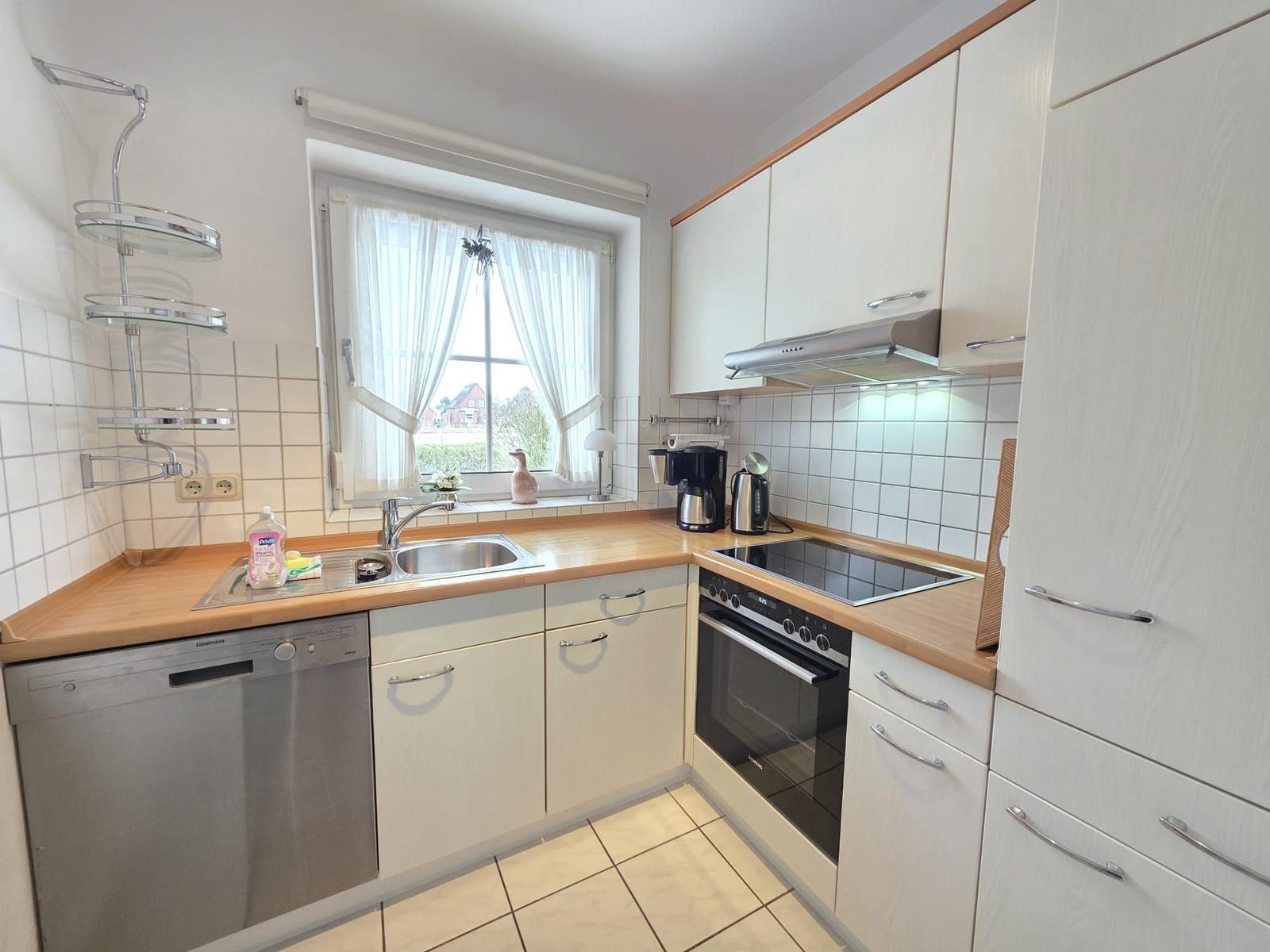 Kitchen with sink, stove, and window with white curtains.