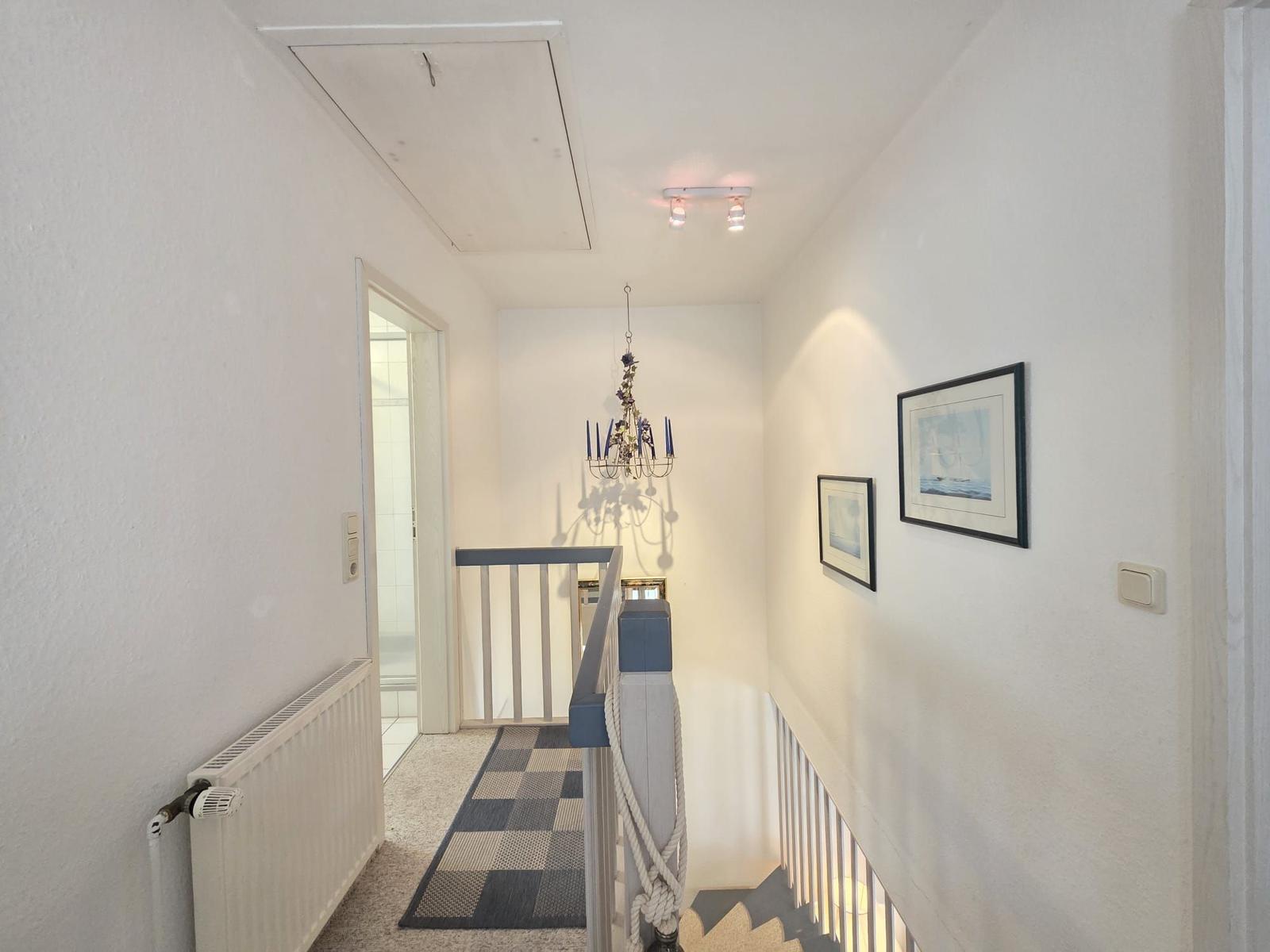 Hallway with stairs, pictures, and chandelier on the wall.
