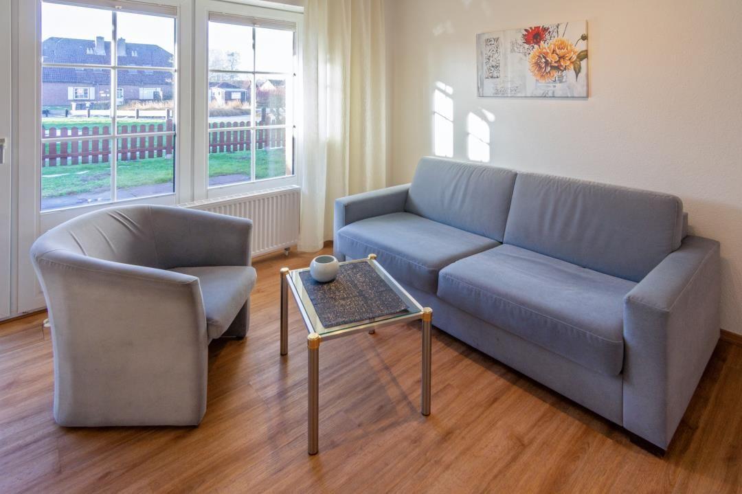 Wohnzimmer mit Sofa, Sessel und Tisch. Fenster mit Blick auf Garten.