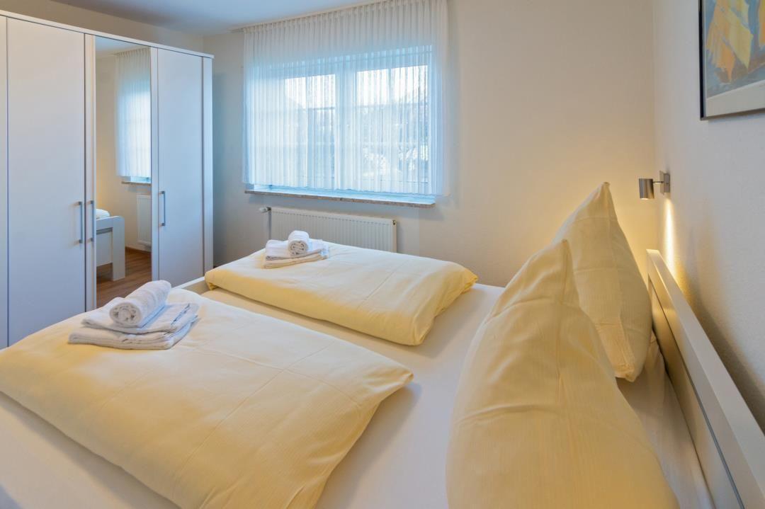 Zwei Betten mit weißen Bettwäschen und Handtüchern. Fenster, Kleiderschrank und Wandbeleuchtung.