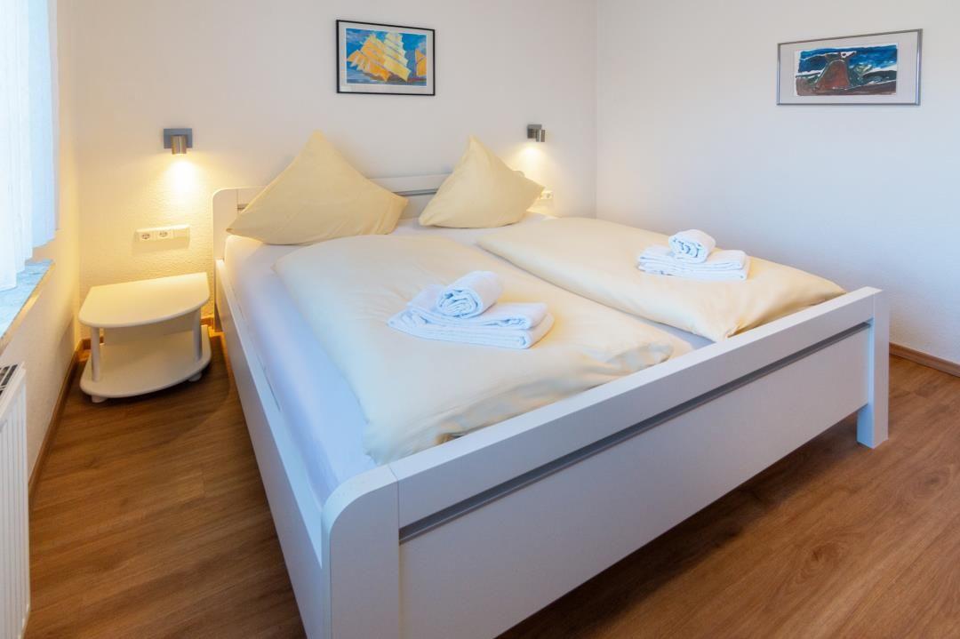Schlafzimmer mit weißem Bett, Holzboden und Wandbildern.