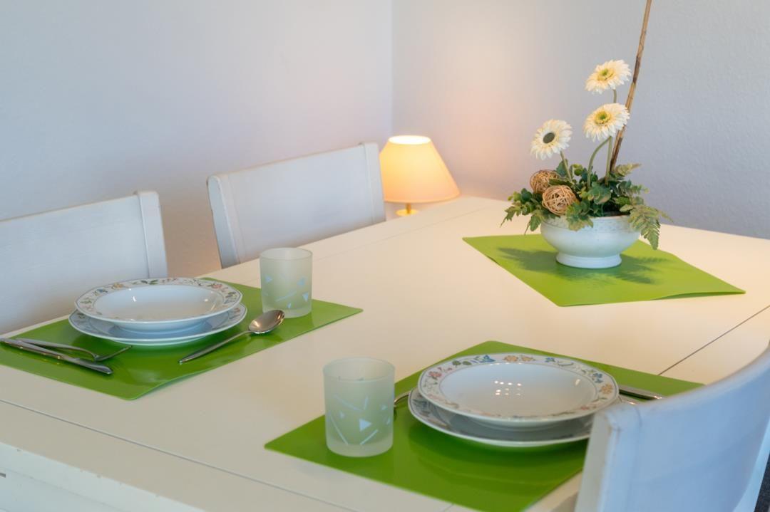 Esstisch mit grünen Untersetzern, Geschirr und Blumenarrangement.