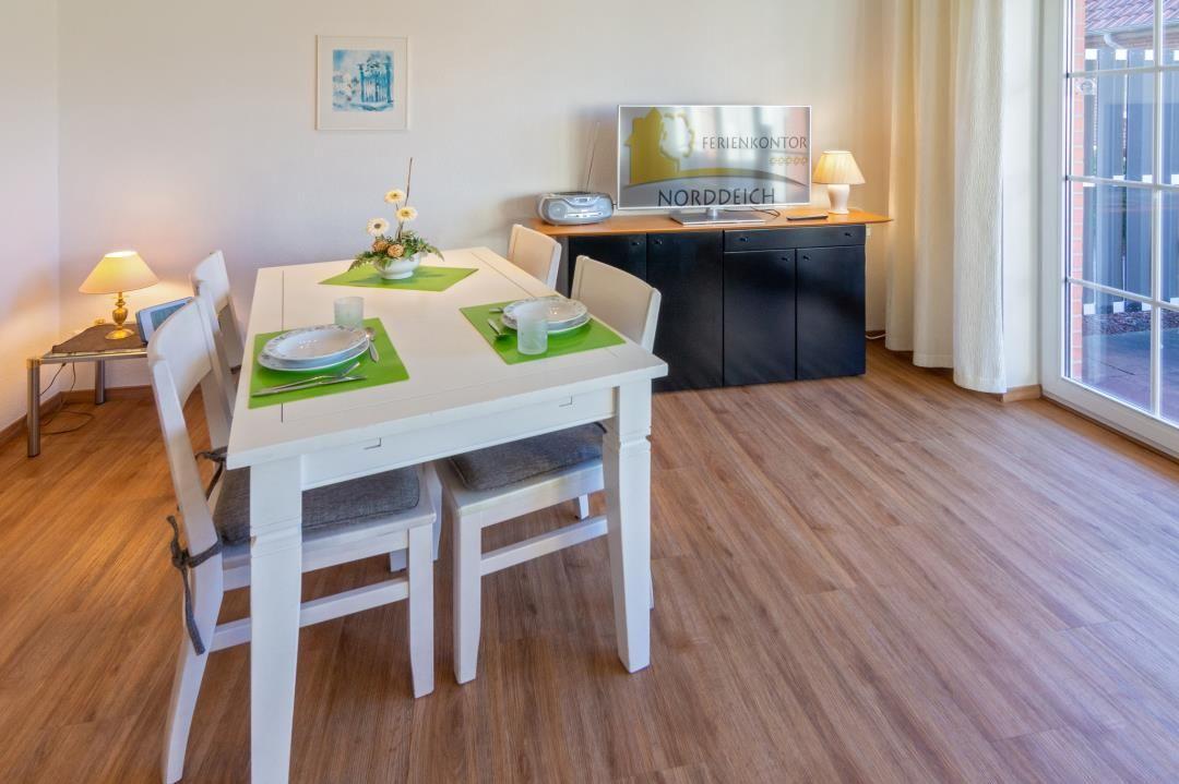 Esstisch mit vier Stühlen, Fernseher und Fenster zur Terrasse.