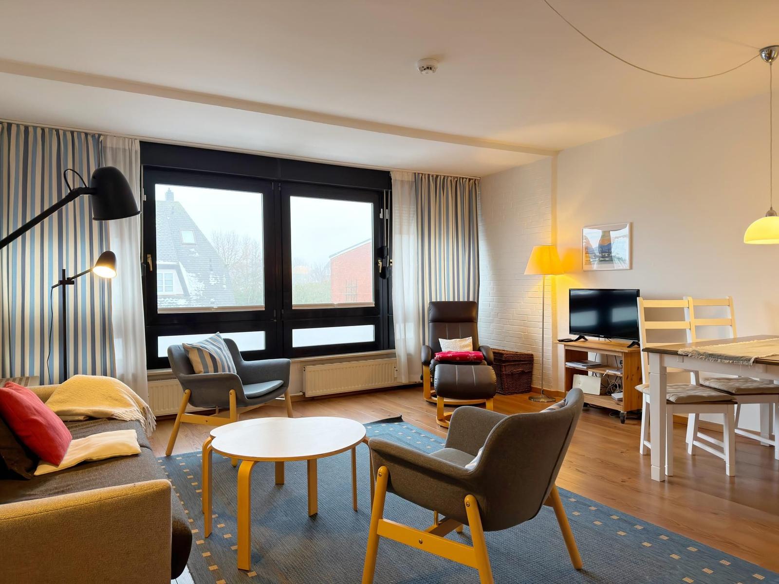 Wohn- und Essbereich mit Sofa, Sesseln und TV. Große Fenster mit Blick.