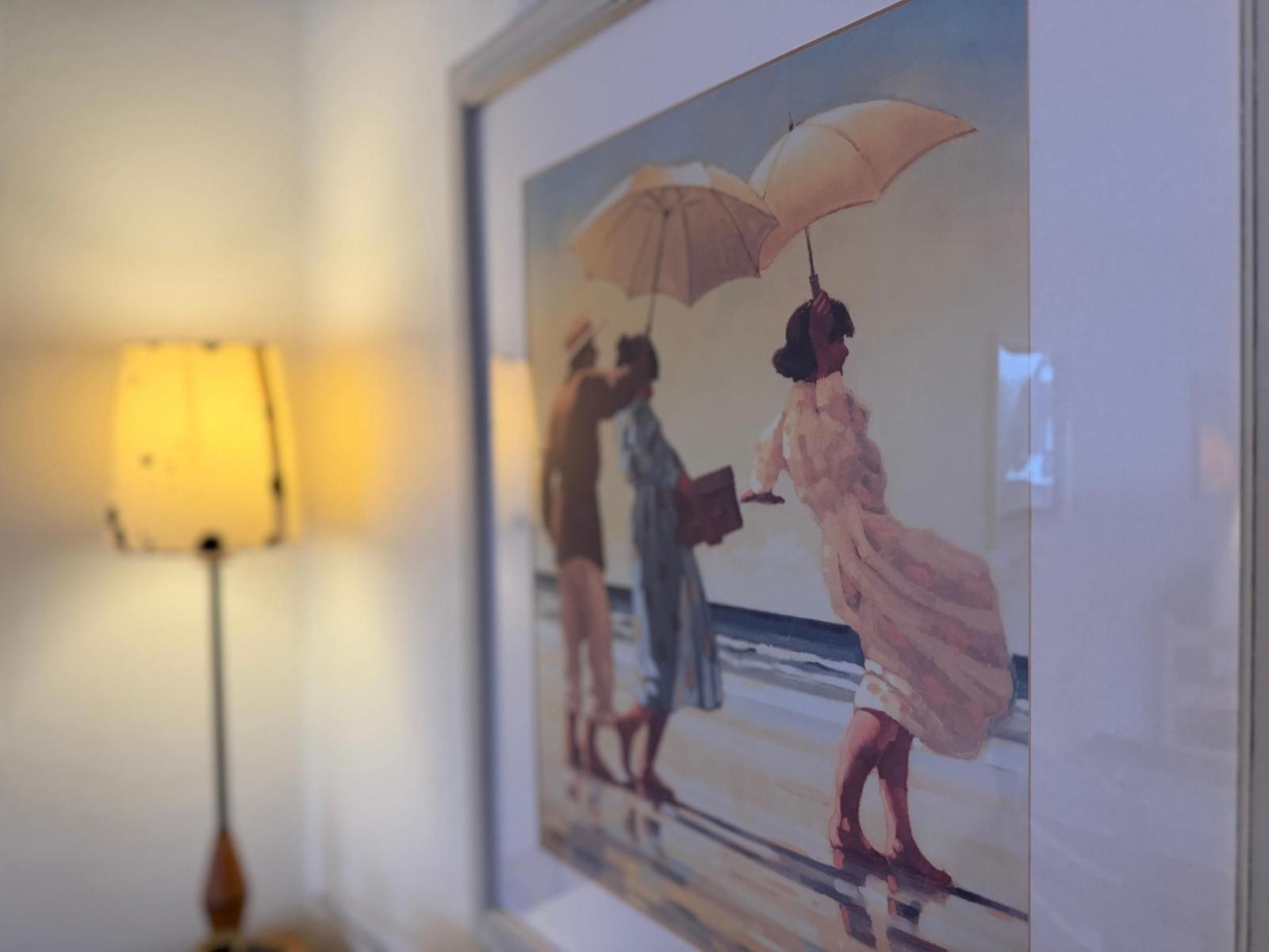 Gelber Stehlampe neben einem gerahmten Bild mit Personen unter Regenschirmen.