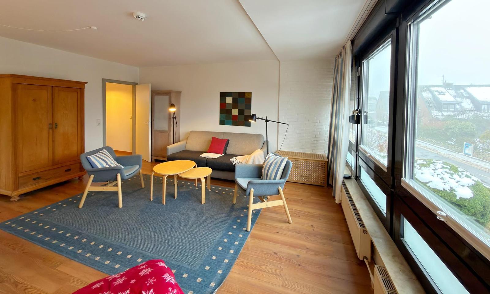 Wohnzimmer mit Sofa, zwei Sesseln und großem Fensterblick