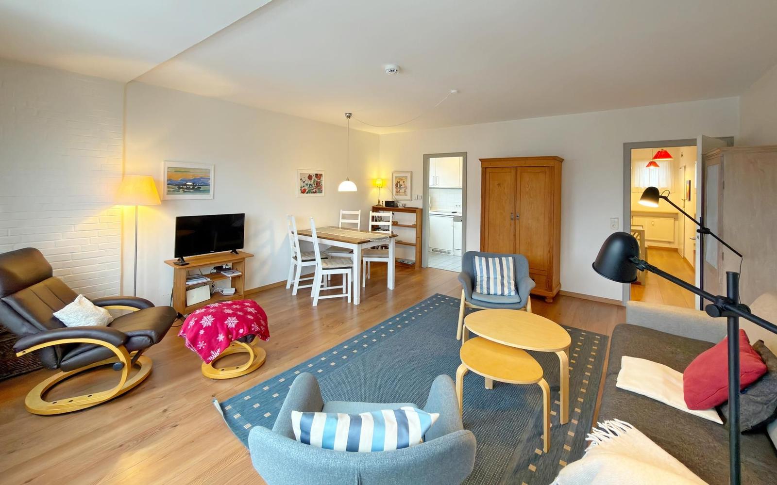 Wohn- und Essbereich mit Holzboden, Sofa, Stühlen und Fernseher.