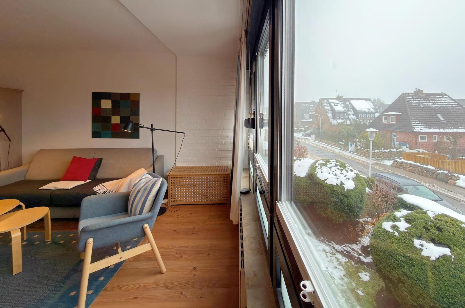 Wohnzimmer mit Sofa, Sessel und großem Fensterblick auf verschneite Gärten.