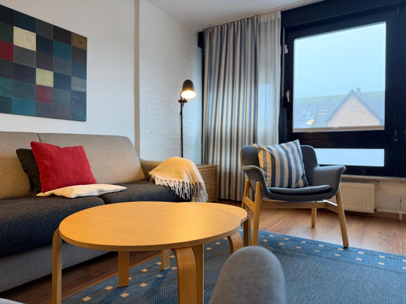 Wohnzimmer mit Sofa, Sessel, Tisch und Blick auf Dach