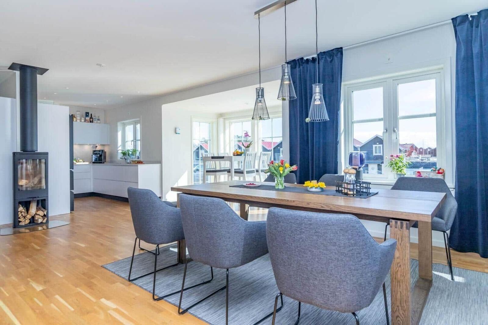 Essbereich mit Holztisch und grauen Stühlen. Küche und Kamin im Hintergrund.