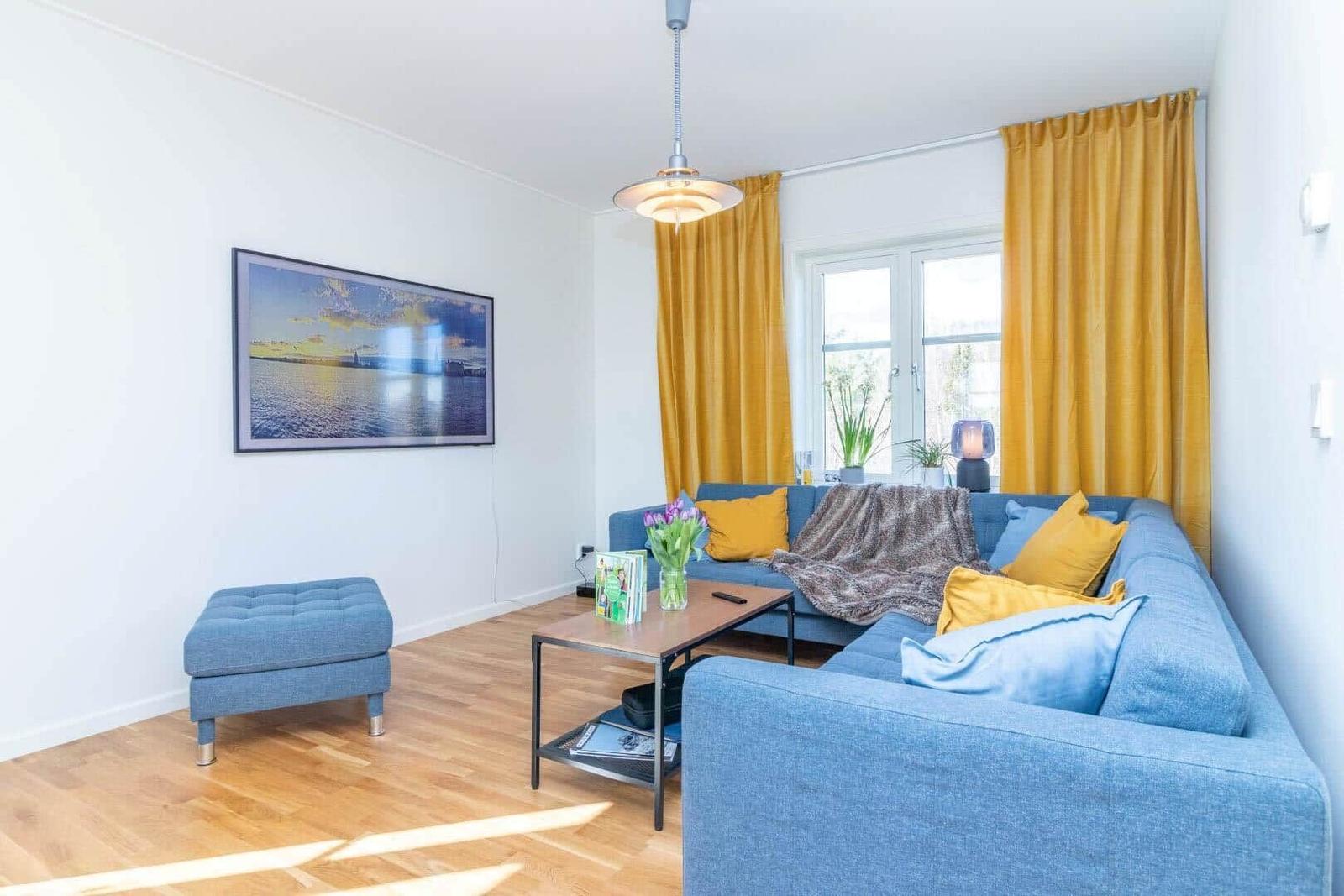Ein Wohnzimmer mit blauem Sofa, gelben Vorhängen und Holzboden.