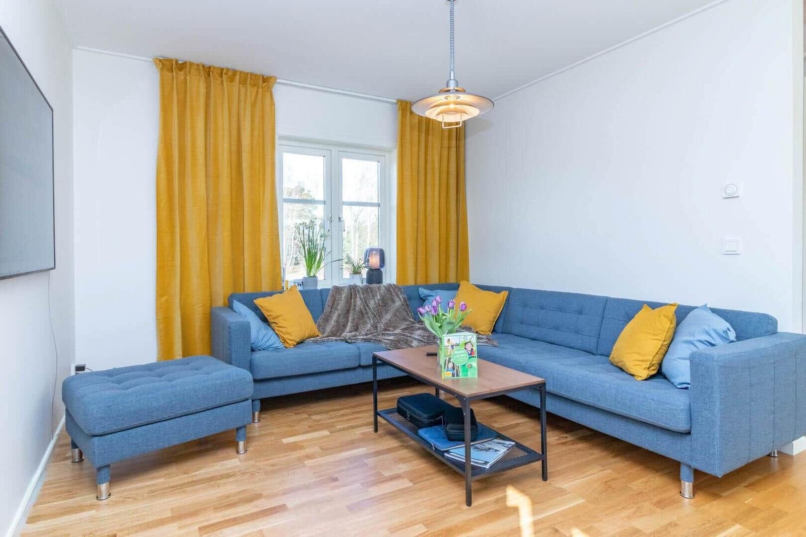 Ein Wohnzimmer mit blauem Sofa, gelben Vorhängen und Holzboden.