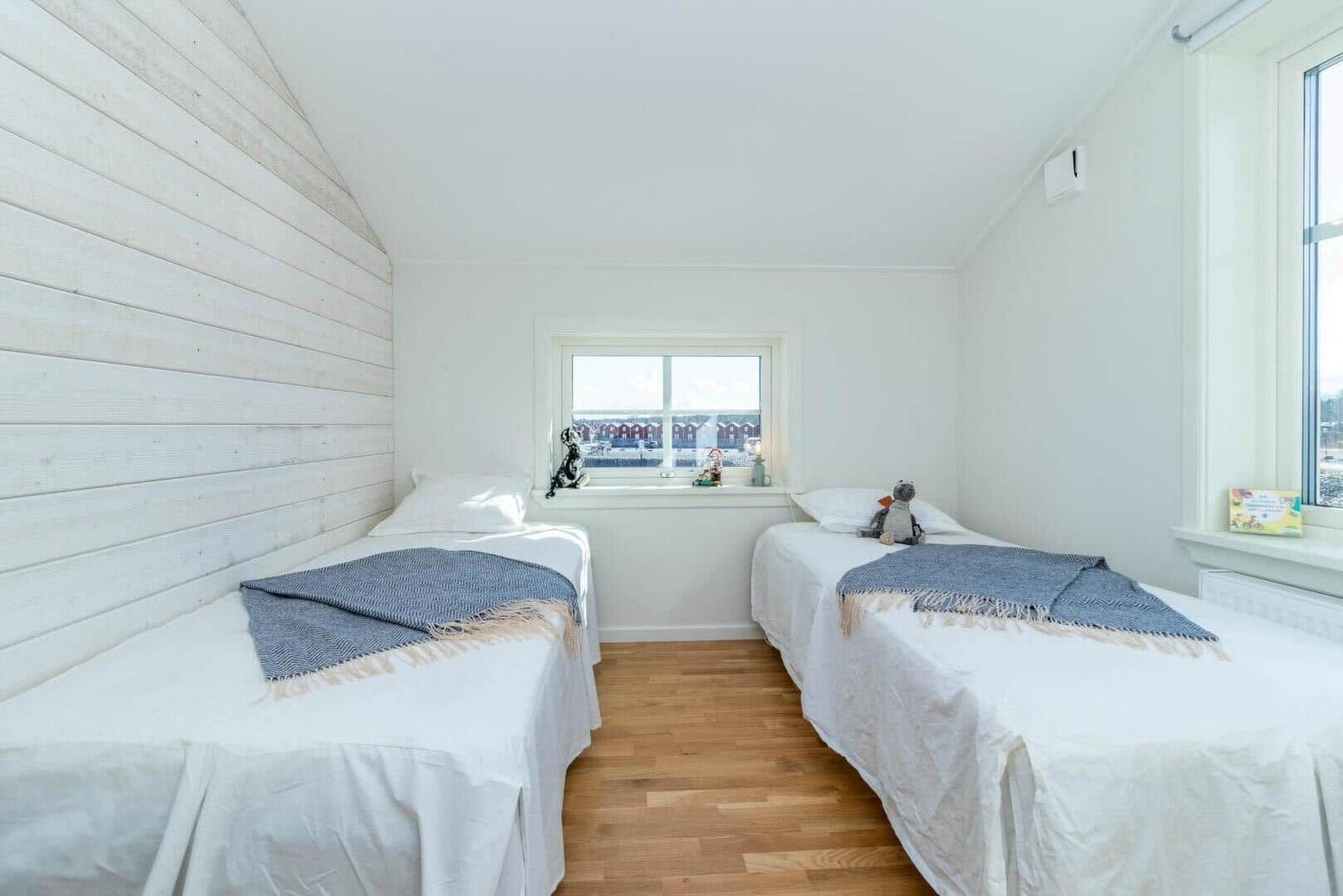 Zwei Betten mit weißen Laken und blauen Decken. Holzfußboden und Fenster mit Blick.