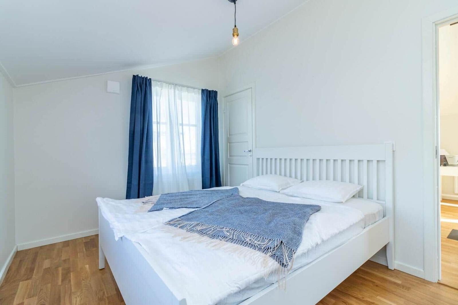 Schlafzimmer mit weißem Bett, blauen Vorhängen und Holzboden.