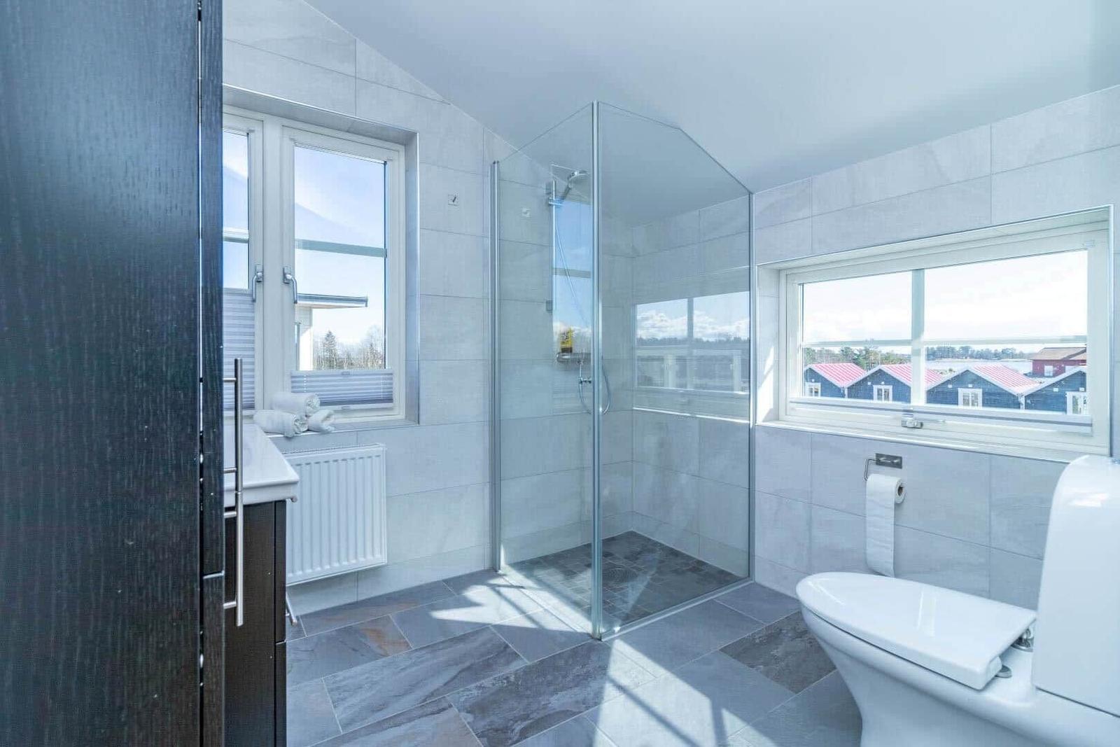 Badezimmer mit Dusche, Toilette und Fenstern zur Aussicht.
