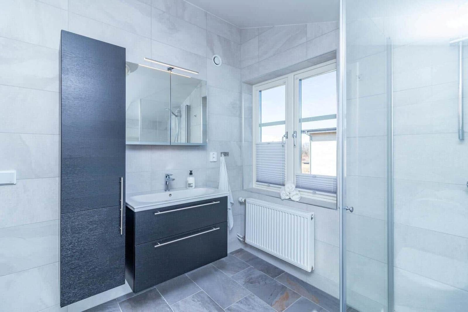 Badezimmer mit Dusche, Waschbecken und Fenster.