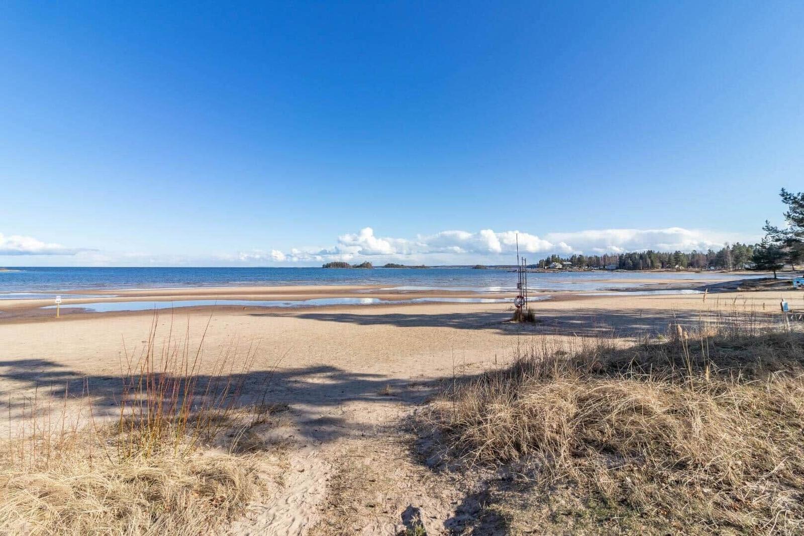 Strand mit Sand, Wasser und blauem Himmel. Ferienhaus direkt am Ufer.
