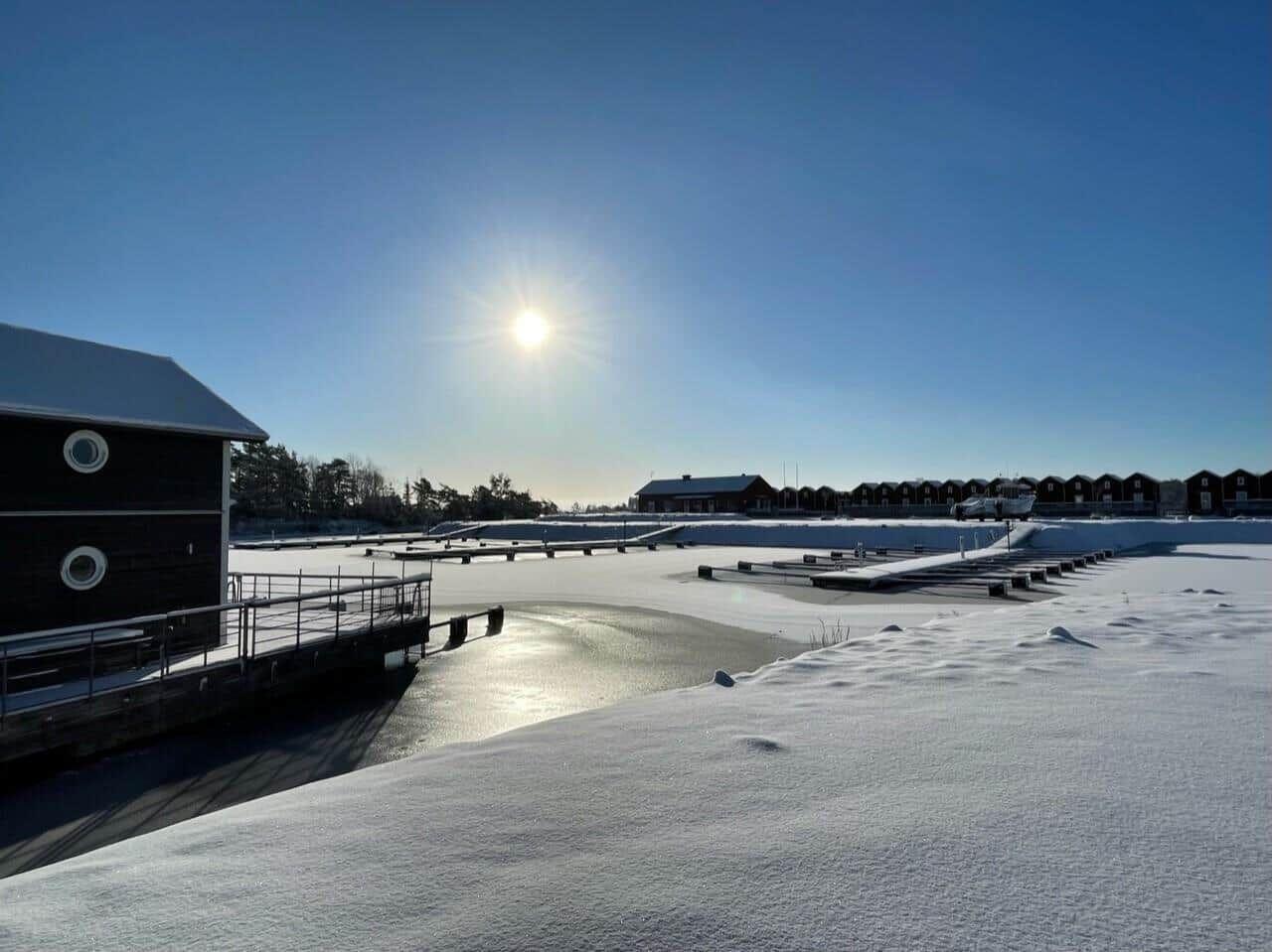 Schneebedeckter Hafen mit Bootshäusern und klarem Himmel.