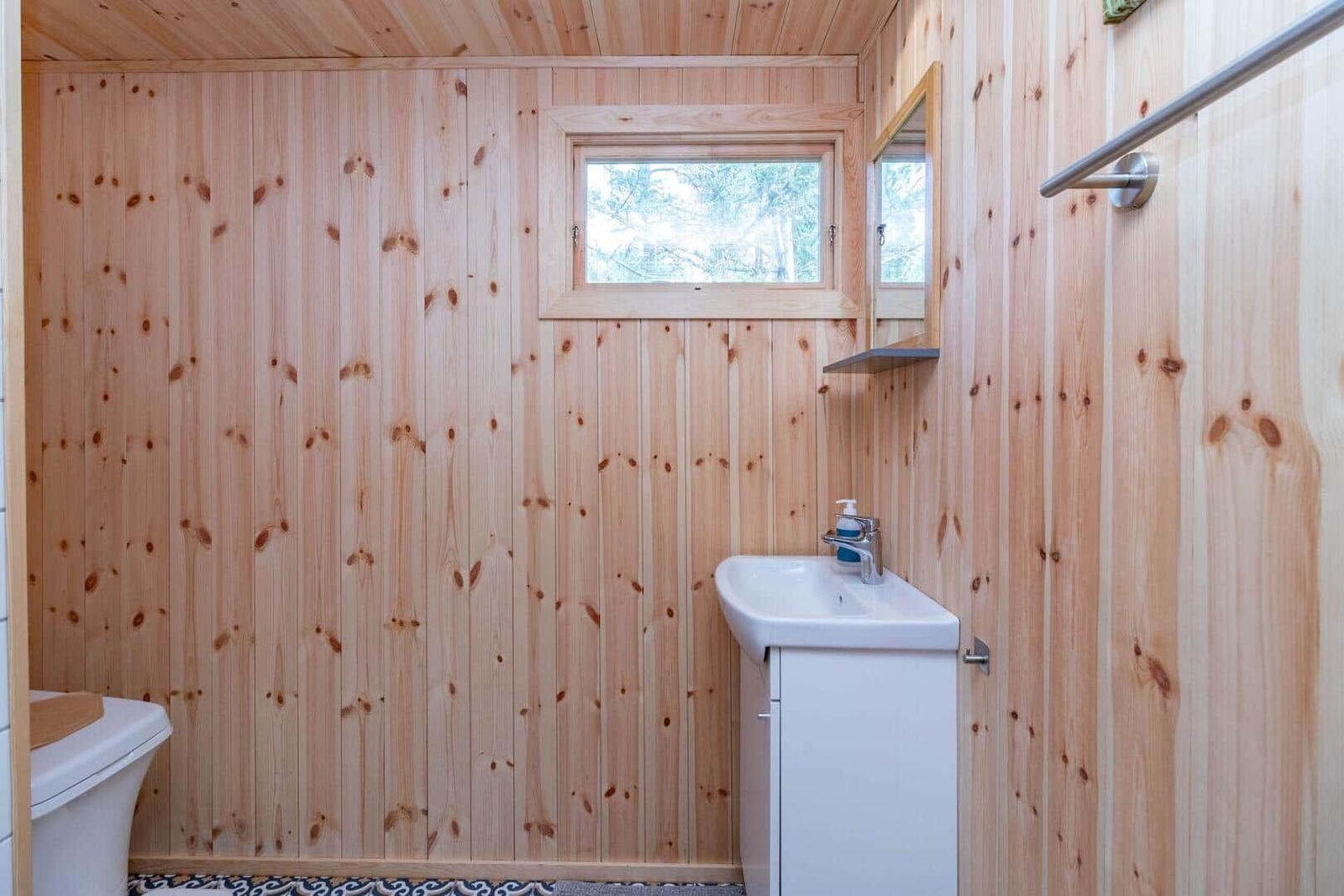Holzbadezimmer mit Waschbecken, Toilette und kleinem Fenster.