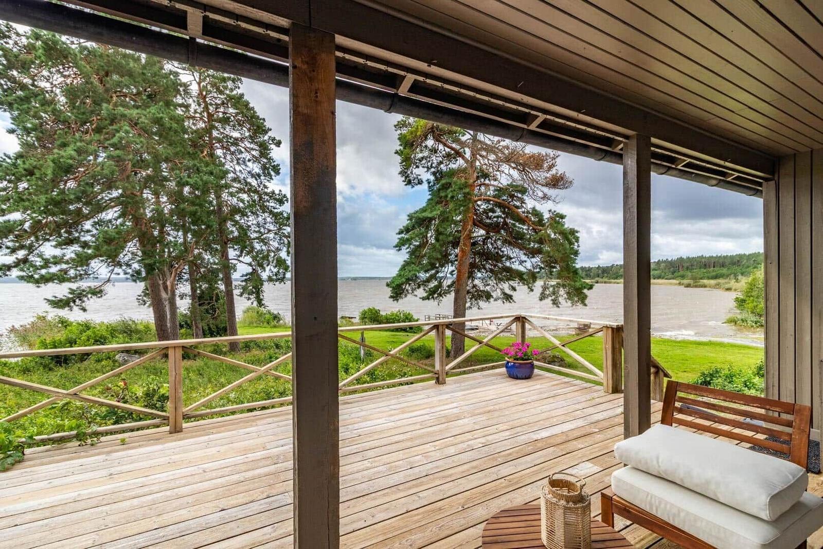 Terrasse mit Blick auf Wasser und Bäume. Holzbank mit Kissen und Pflanze.