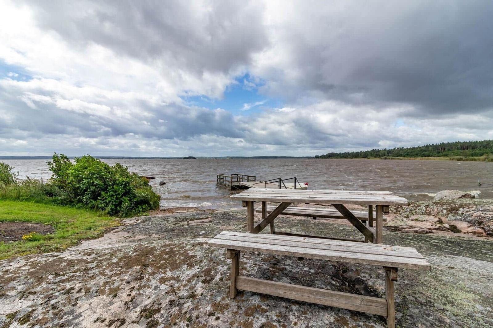 Holztisch und Bänke auf Steinufer mit Blick auf See und Himmel.