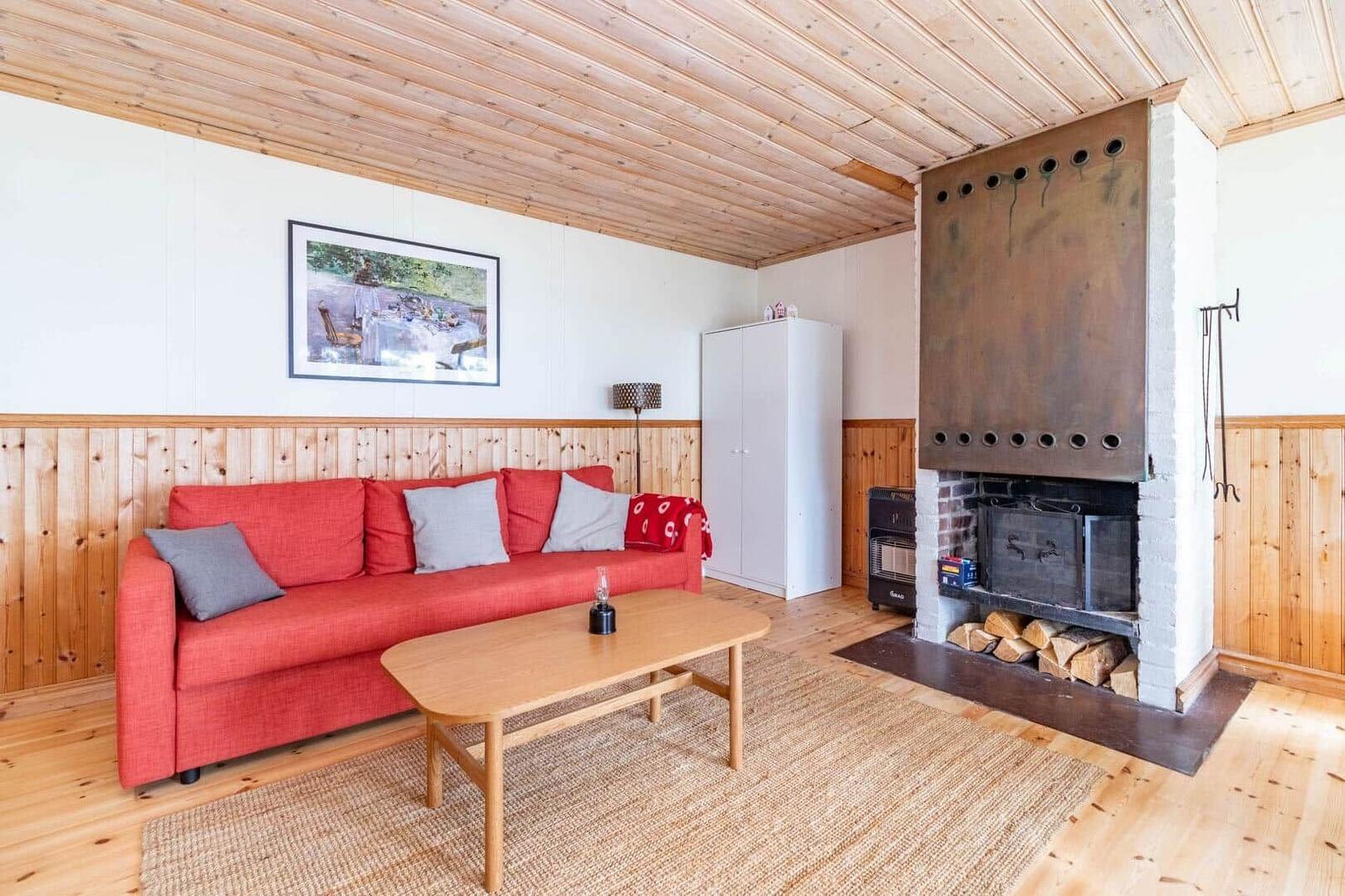 Ein Wohnzimmer mit rotem Sofa, Holzdecke und Kamin mit Holz.