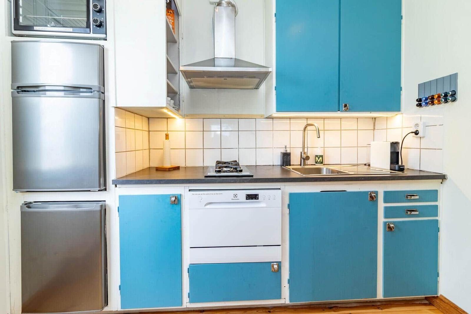 Küche mit blauen Schränken, Edelstahlgeräten und weißer Fliesenwand.